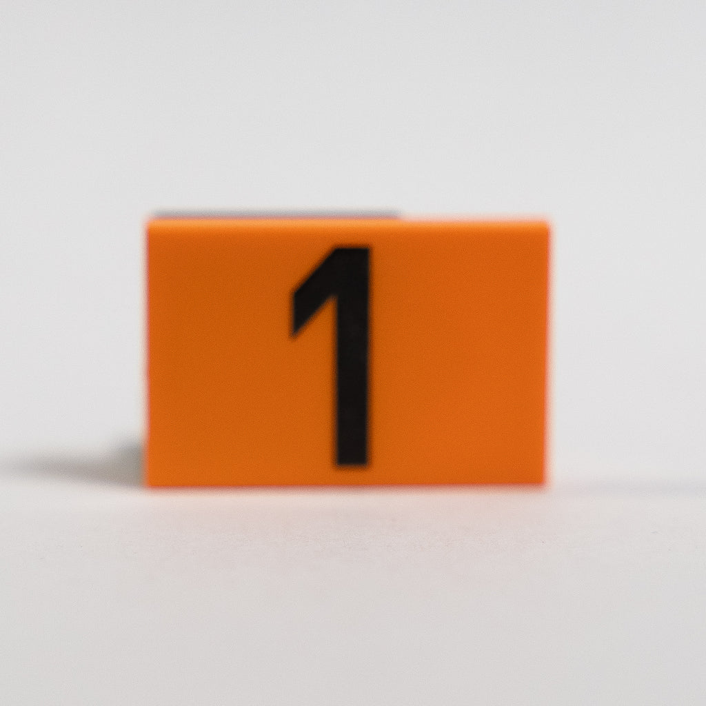 An orange 2x3 LEGO Tile photographed on a white background, with the number 1 printed in black.