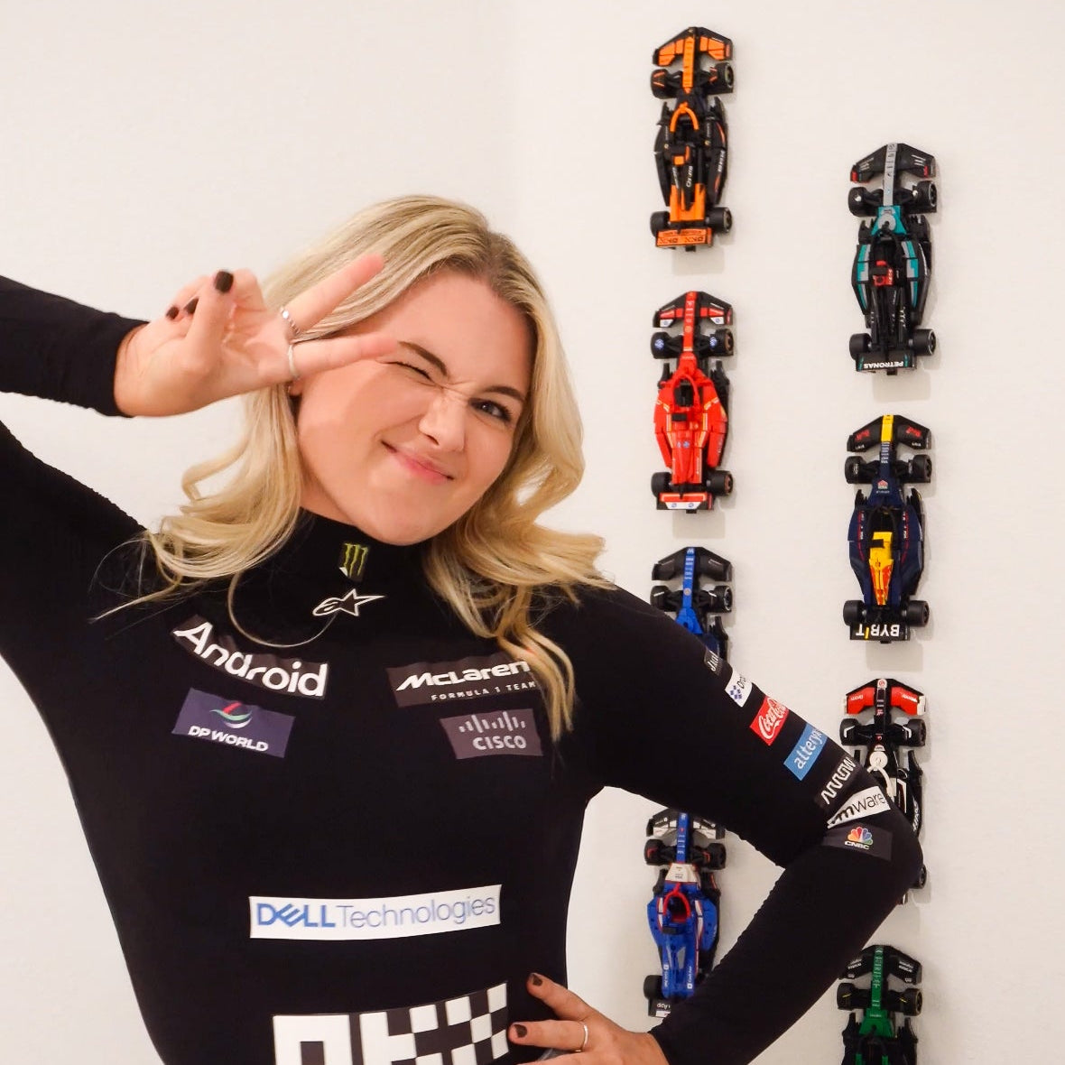 Person wearing a black long-sleeve shirt with logos and denim shorts, posing in front of a wall of lego cars.