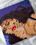 A square custom LEGO-style portrait mosaic built on a white fabric background, showing a close-up face with brown hair, beige skin tones, dark brown clothing, and purple accents.